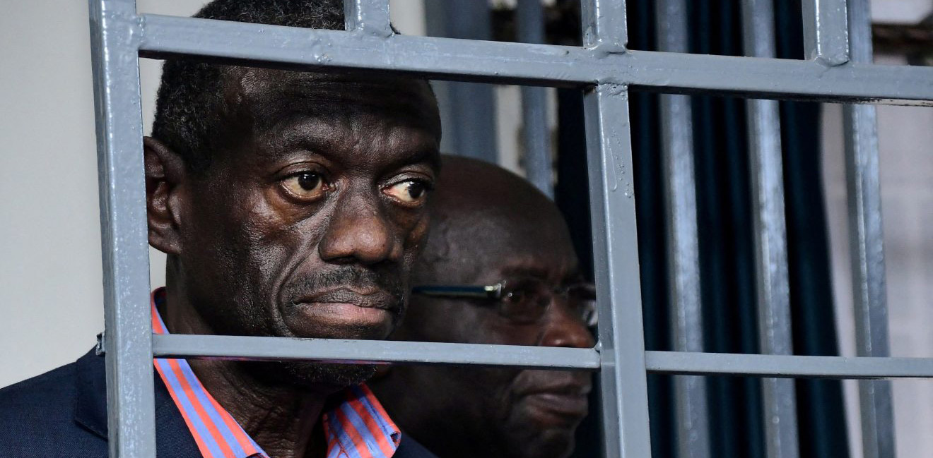 Kizza Besigye seated behind bars in a courtroom dock